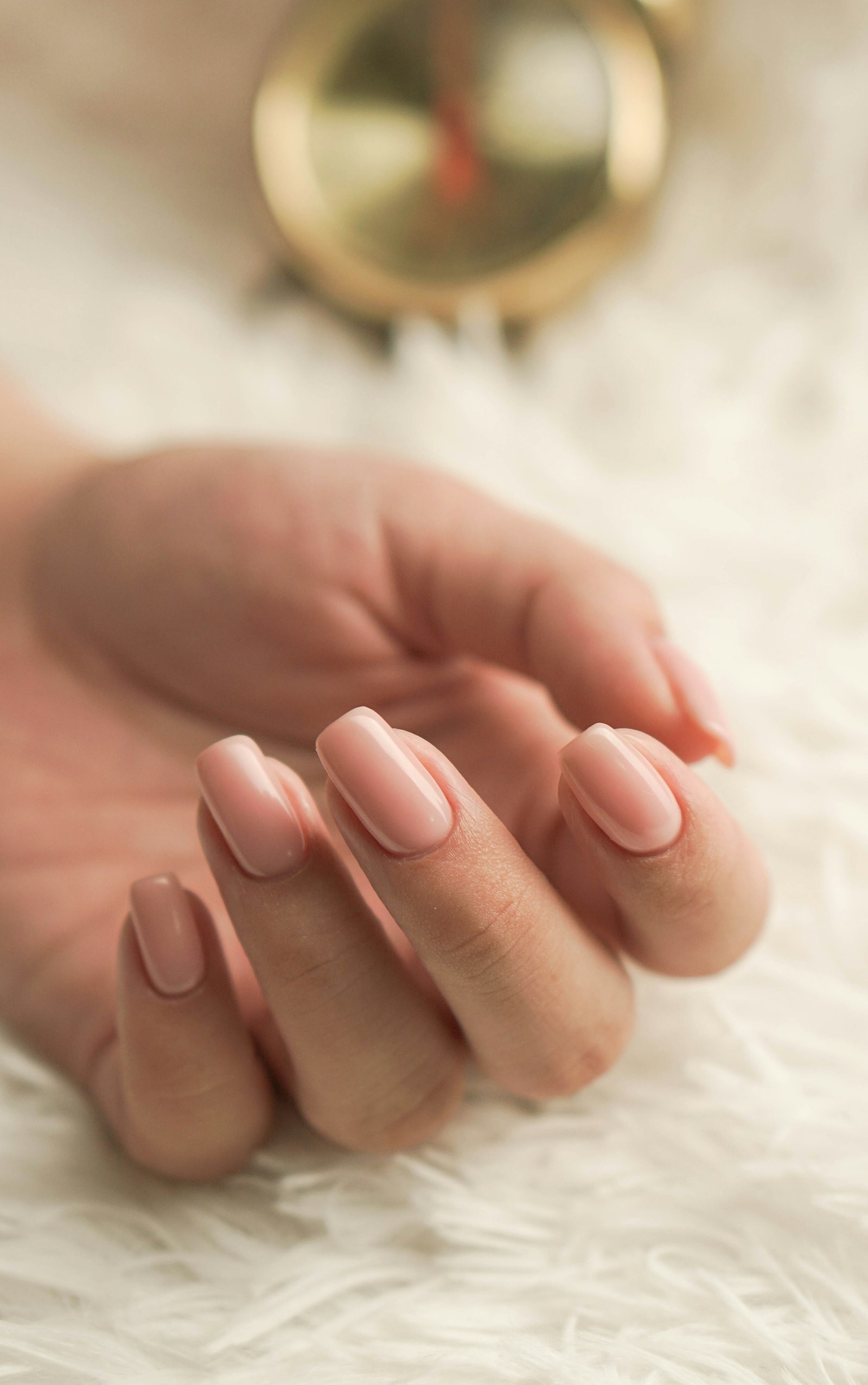 Mão feminina com unhas em tom nude e acabamento delicado