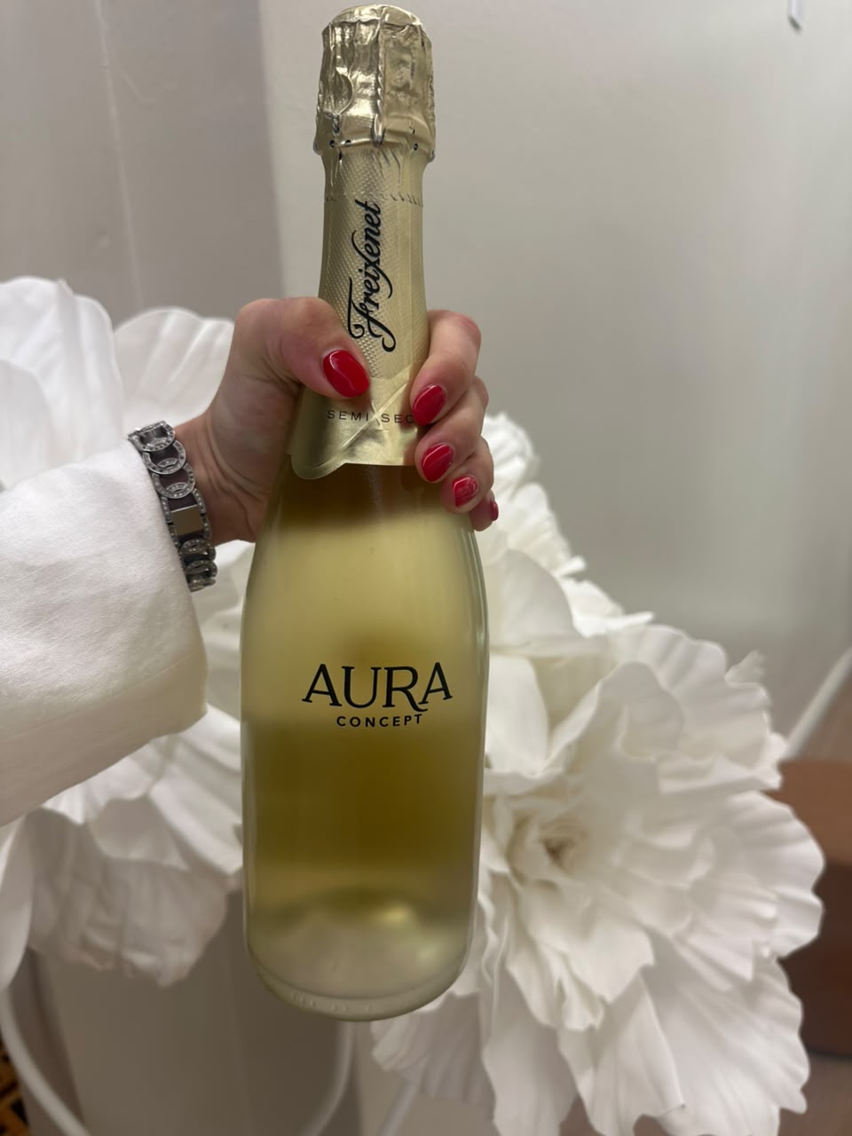 Mão com unhas vermelhas segurando uma garrafa de espumante personalizada Aura Concept