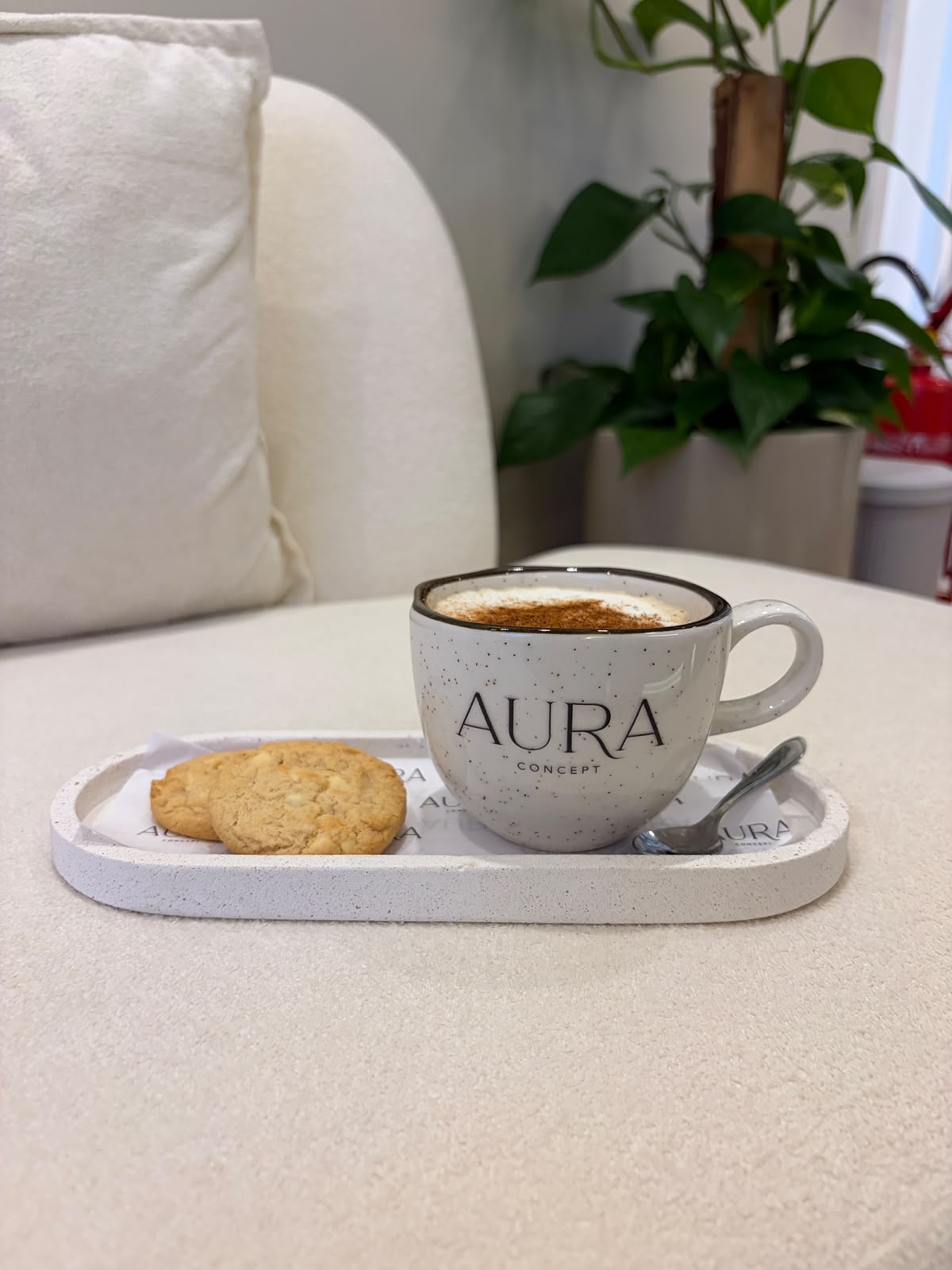 Xícara de café com a marca Aura Concept e biscoitos em uma bandeja