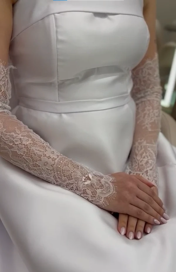 Detalhe do vestido de noiva com luvas de renda e mãos apoiadas no colo
